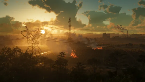 A field burning at sunset under power lines, smokestacks beyond.