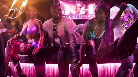 Seated with dancers and cash in the club, a Jack of Hearts banner on the wall behind.