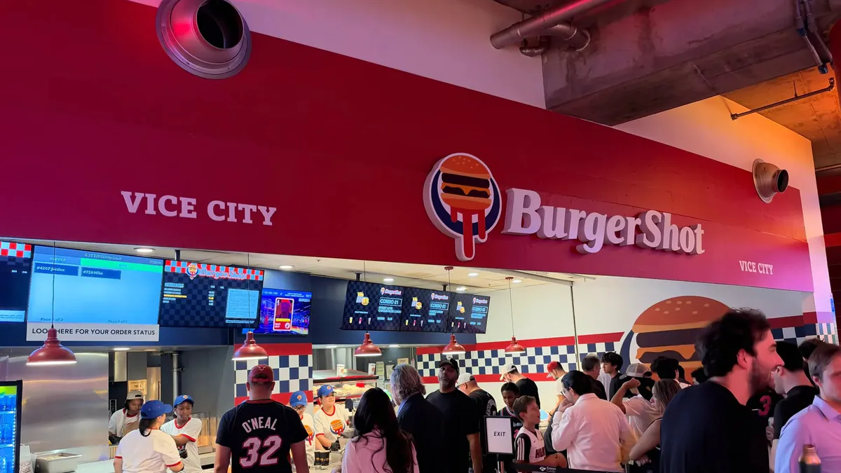 The BurgerShot counter at Miami’s Kaseya Center displays the BurgerShot sign above digital menu boards and a queue of customers.