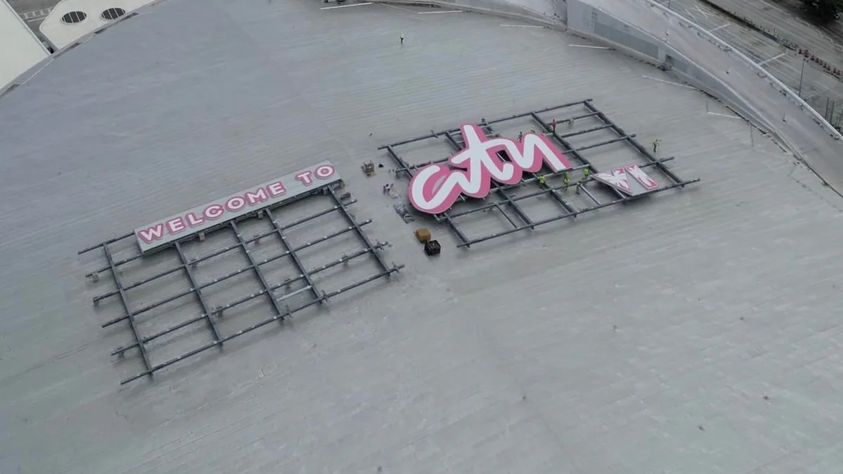 Seen from above, “Welcome to” and the pink “Vice City” lettering sit on scaffolding frames on an arena roof, a causeway to the port behind.