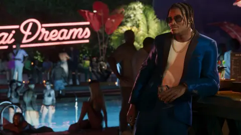 In a blue suit jacket at a nighttime pool party, leaning on the bar.