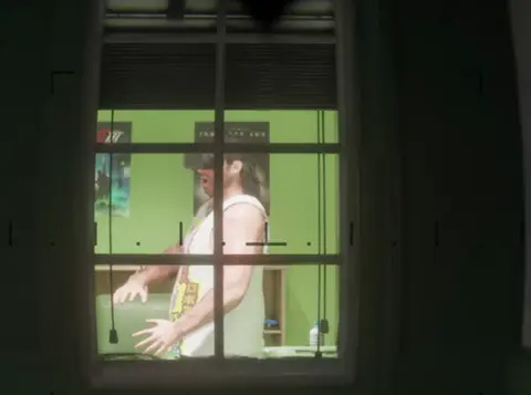 Through binoculars: a man in a VR headset in a green room.