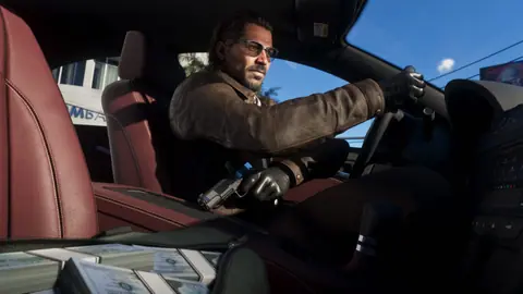 Driving in leather gloves with a pistol held low, stacks of cash on the passenger seat.