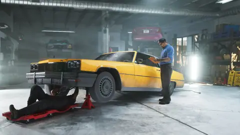 A yellow car on jack stands at a shop, a mechanic underneath on a creeper.